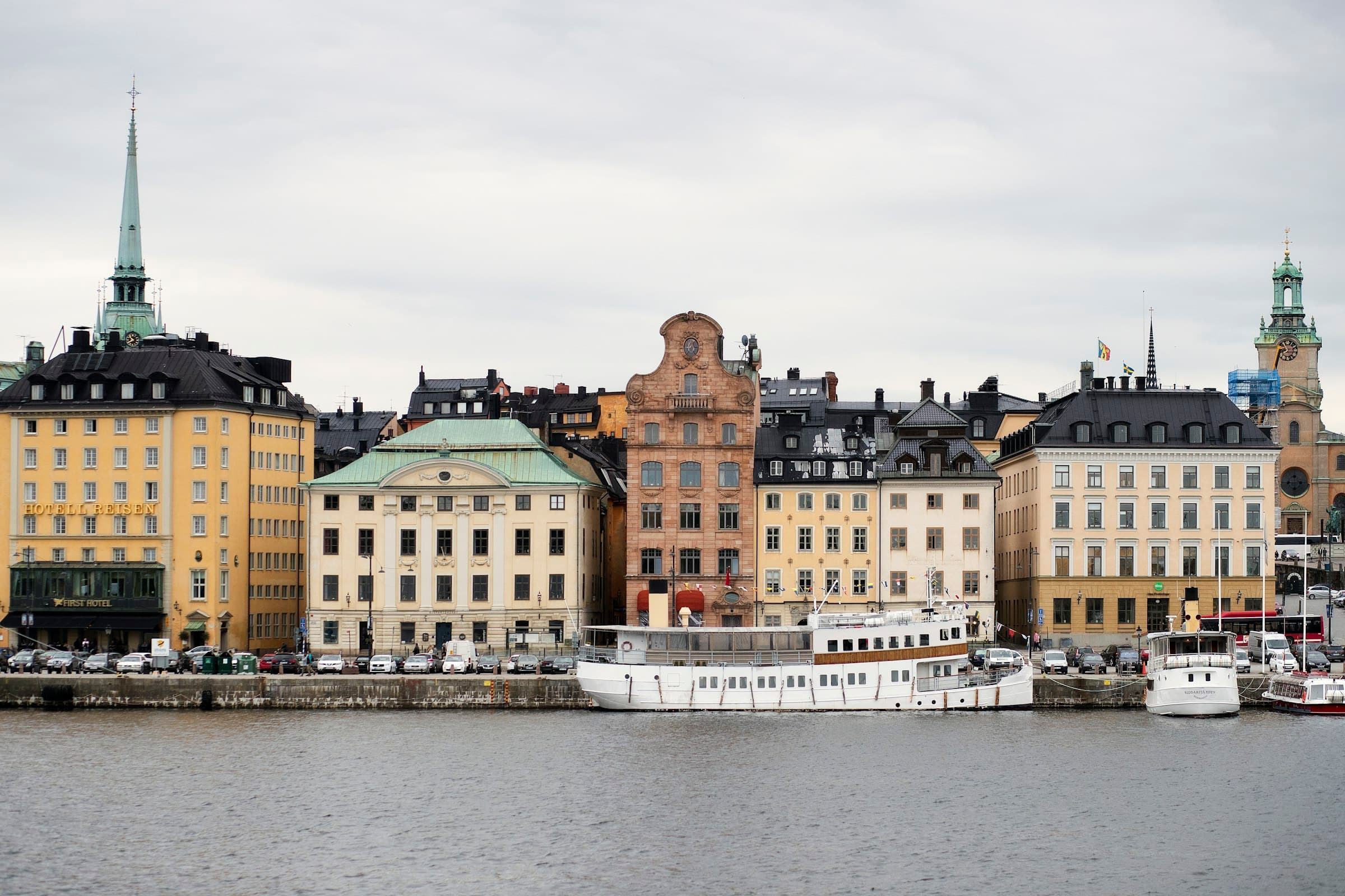 Gamla Stan, Stockholm’s old town: pastel merchant houses and a church spire along the Skeppsbron quay, with boats moored in front