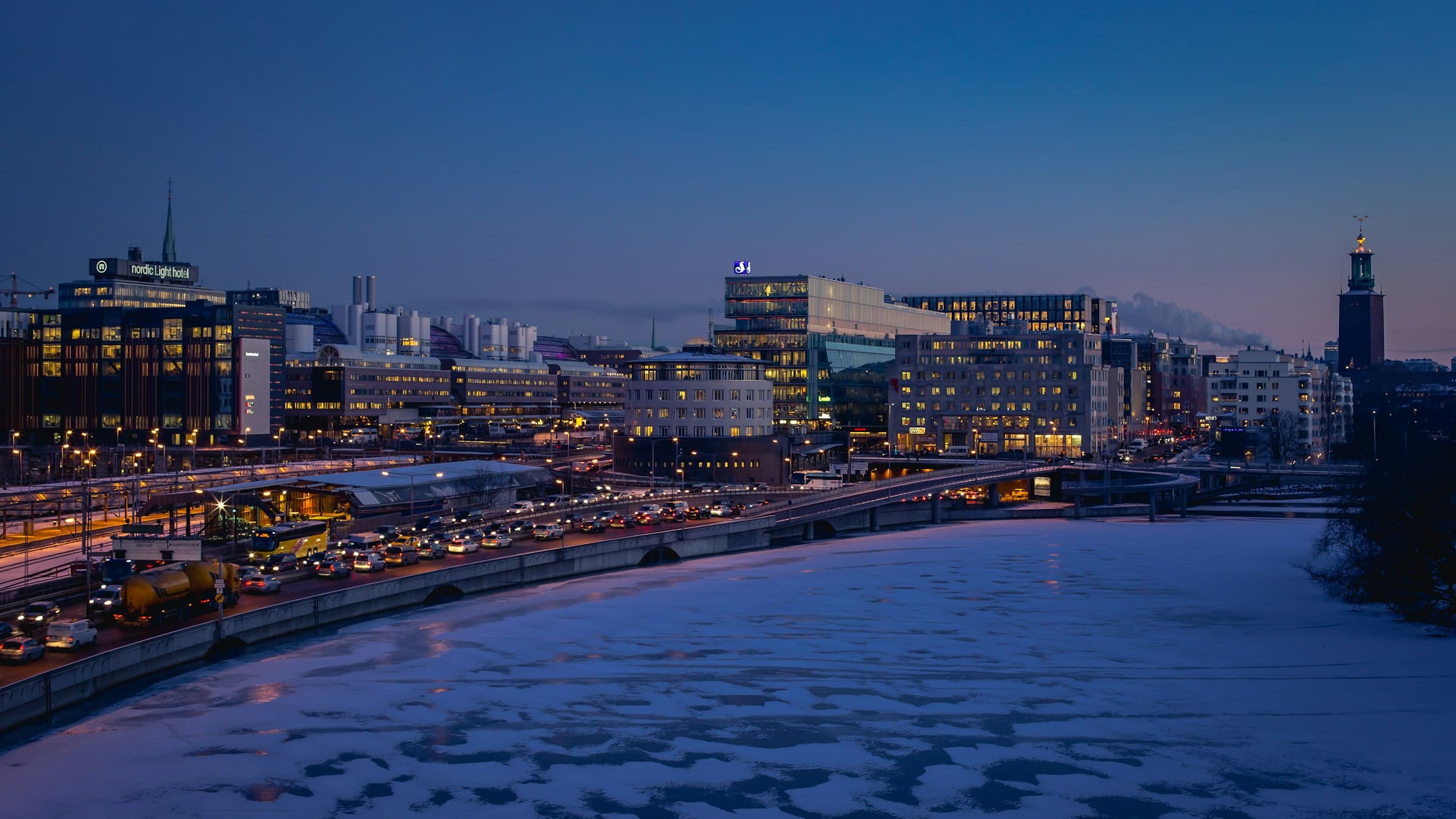 Central Stockholm at dusk: office buildings and city lights along the water, seen from a bridge in winter