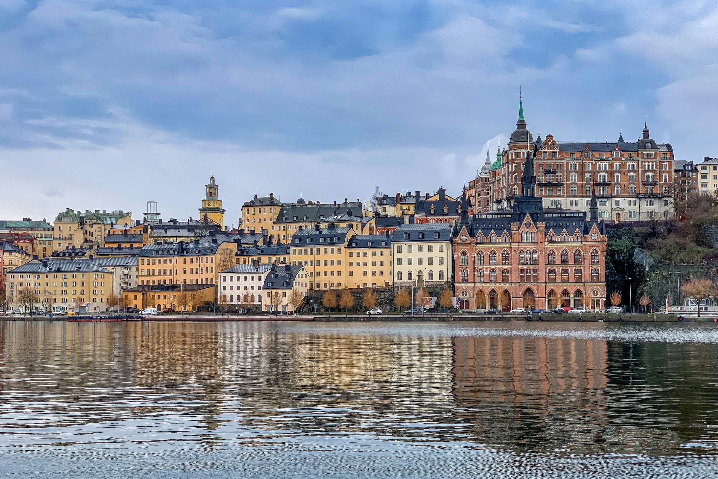 The Stockholm waterfront at Södermalm: ochre and red-brick facades and church spires reflected in still water under a pale sky