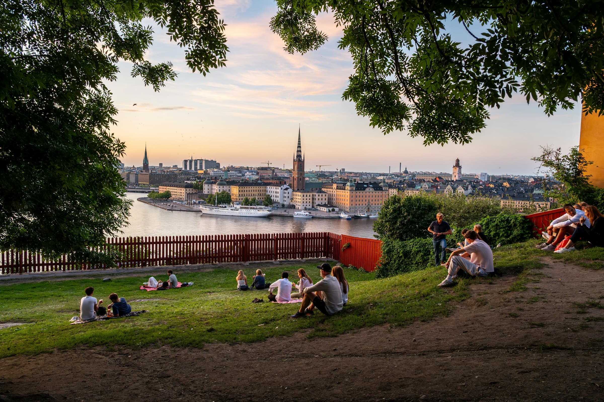 People relaxing on the grass at Skinnarviksberget on a summer evening, overlooking Stockholm and the water